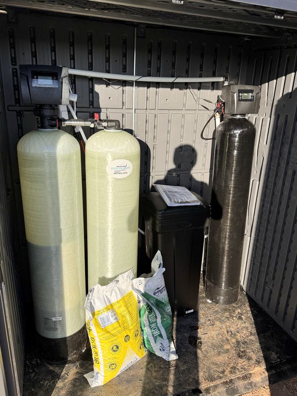 Outdoor well water system in a weatherproof enclosure: a two-tank iron filter on the left, a water softener and its brine tank on the right